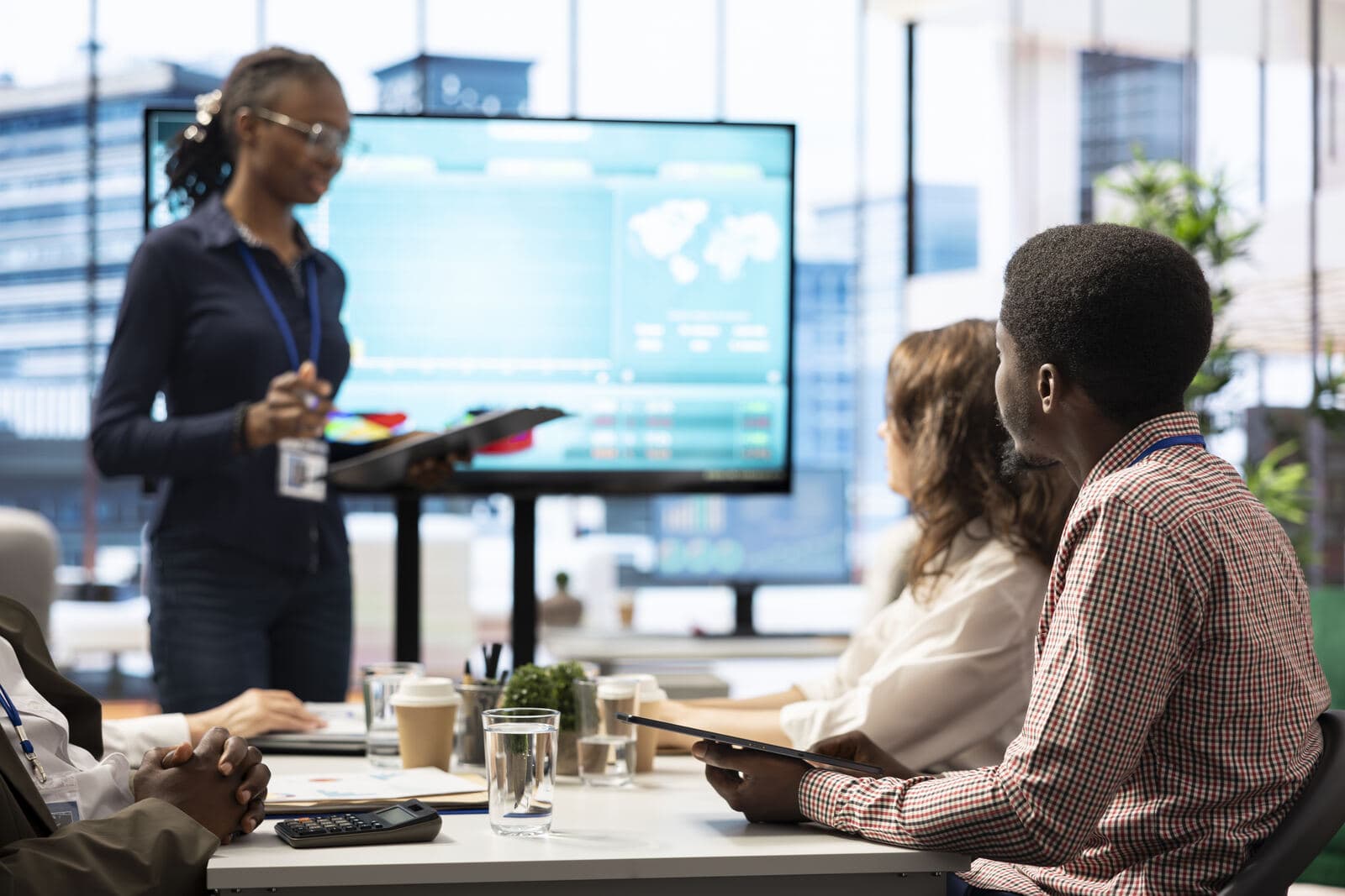 Colleagues around a meeting table, one presenting at a screen