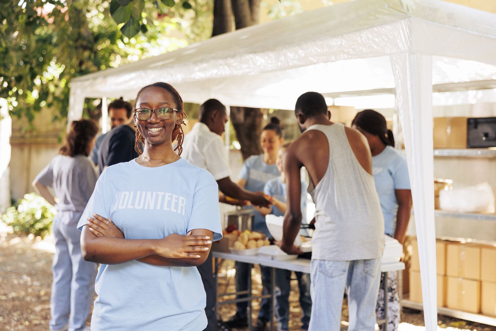 A volunteer smiling at a community food stall, with others serving behind her